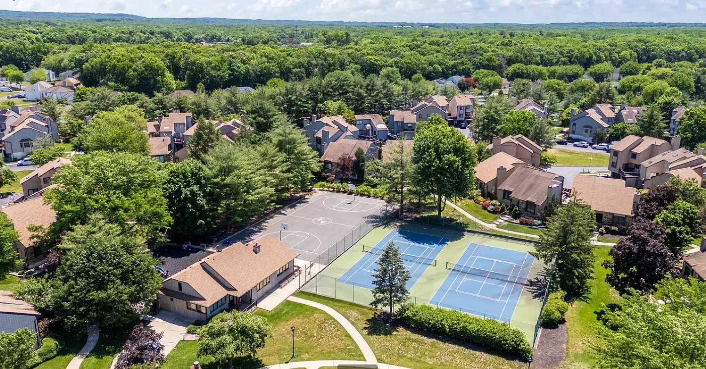 Aerial view of the Foxborough Village clubhouse, tennis court, and basketball court among the townhomes and trees.
